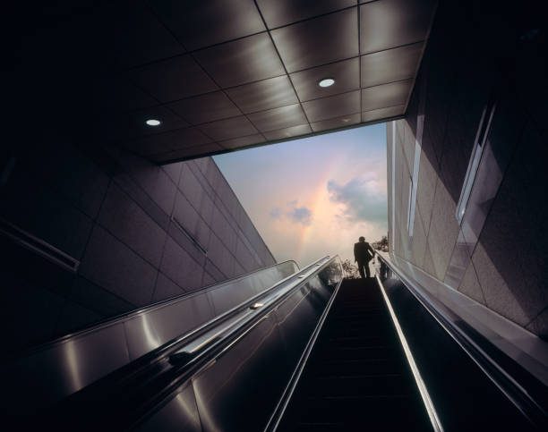 Escalator of subway station with businessman moving towards dramatic sky with rainbow.